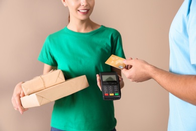 Photo of Young man with credit card using bank terminal for delivery payment on color background, closeup