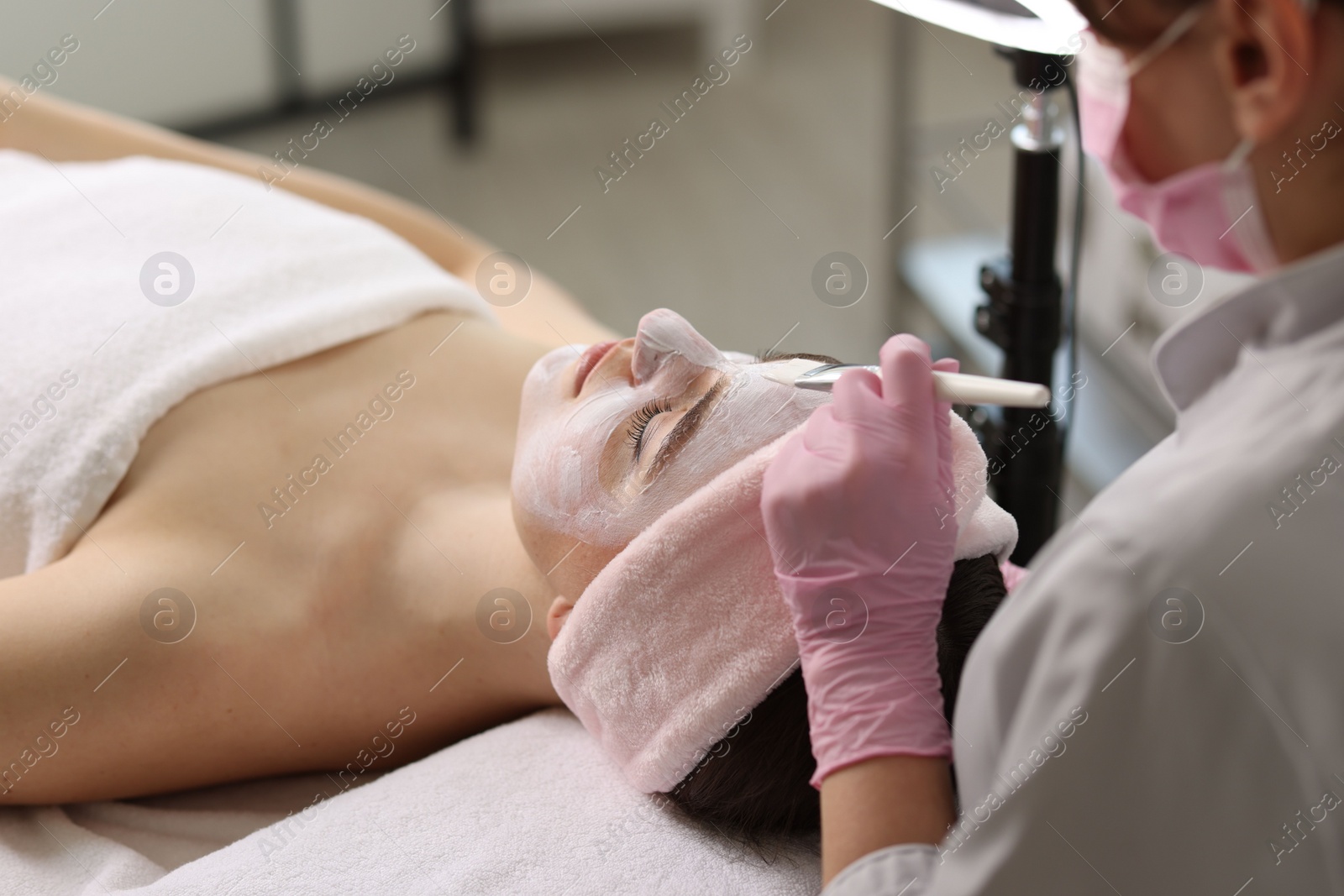 Photo of Cosmetologist applying mask on woman's face in clinic, closeup