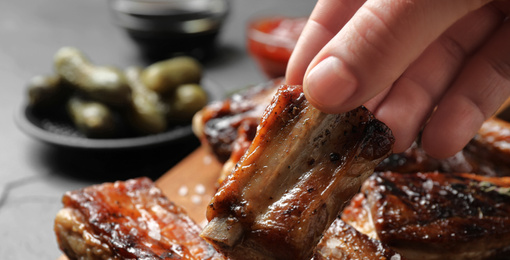 Woman with tasty grilled ribs at table, closeup. Banner design