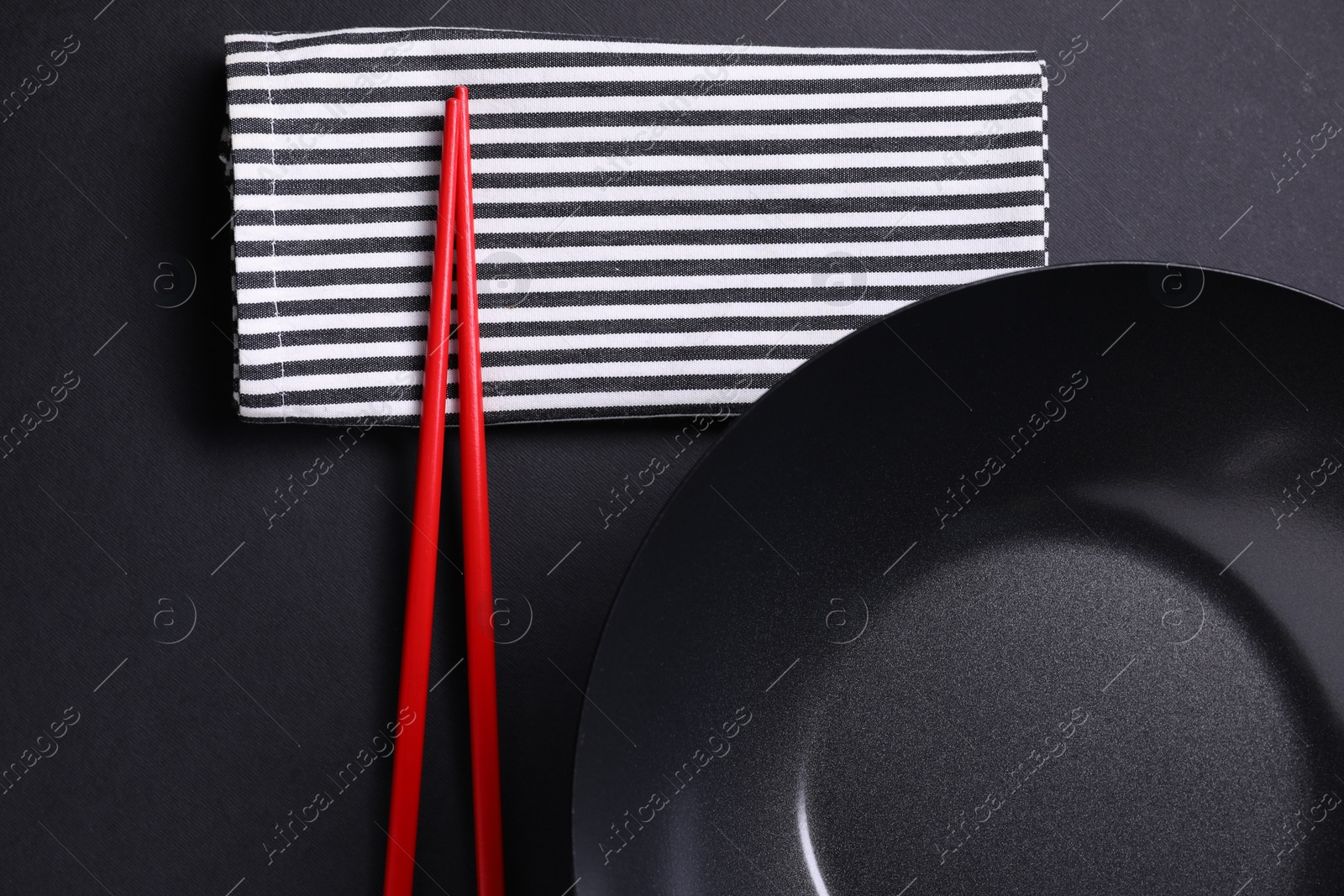 Photo of Empty iron wok and chopsticks on black table, flat lay