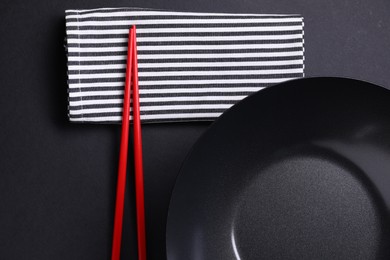 Empty iron wok and chopsticks on black table, flat lay