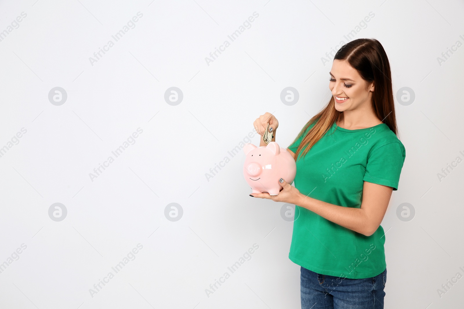 Photo of Young woman putting money into piggy bank on white background. Space for text