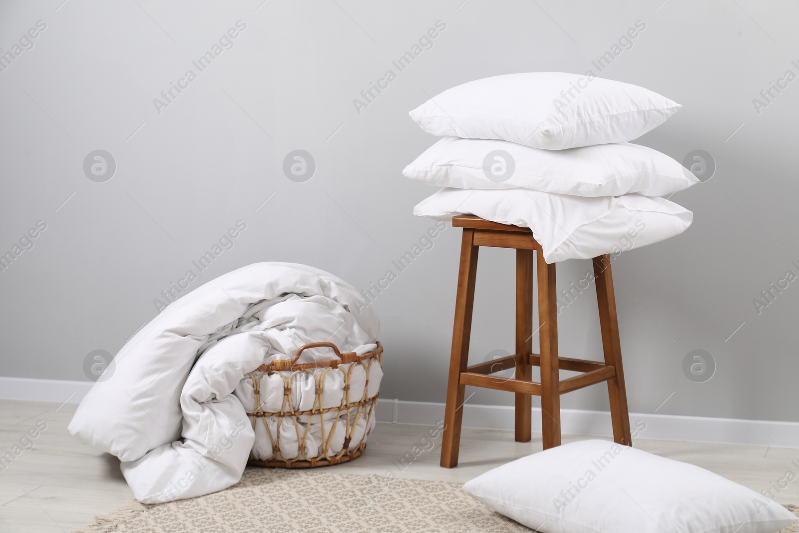 Photo of Soft pillows, duvet and chair near light grey wall indoors