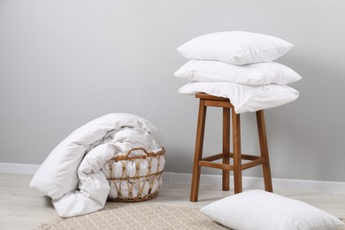 Soft pillows, duvet and chair near light grey wall indoors