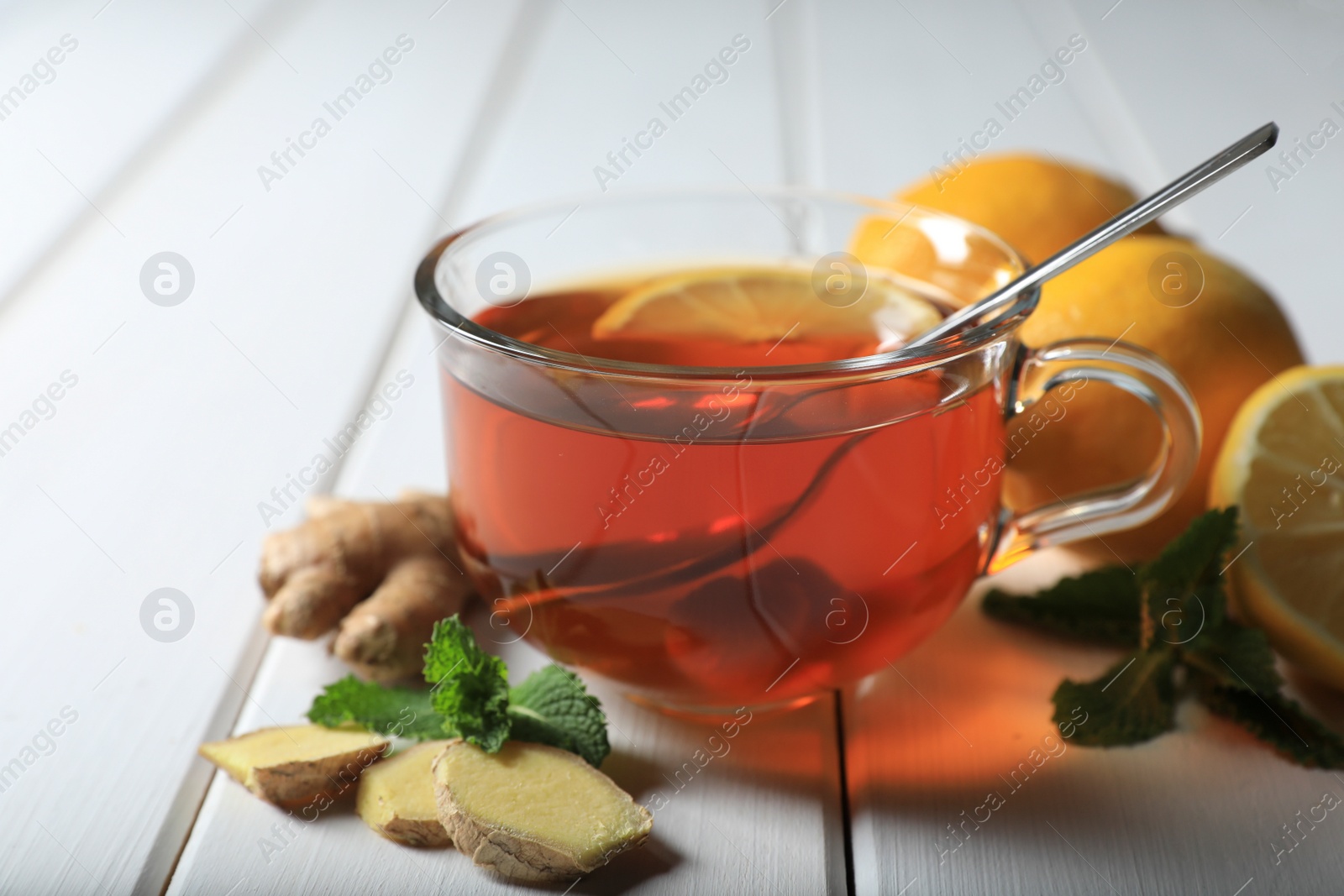 Photo of Cup of delicious ginger tea and ingredients on white wooden table, closeup