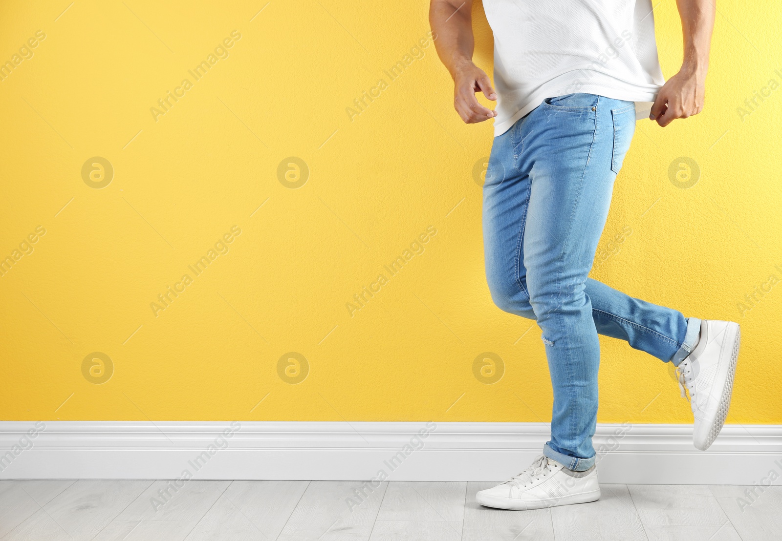 Photo of Young man in stylish jeans near color wall with space for text, focus on legs