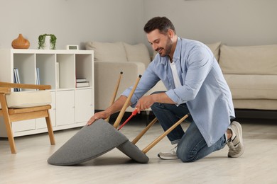 Photo of Man with screwdriver assembling armchair on floor at home