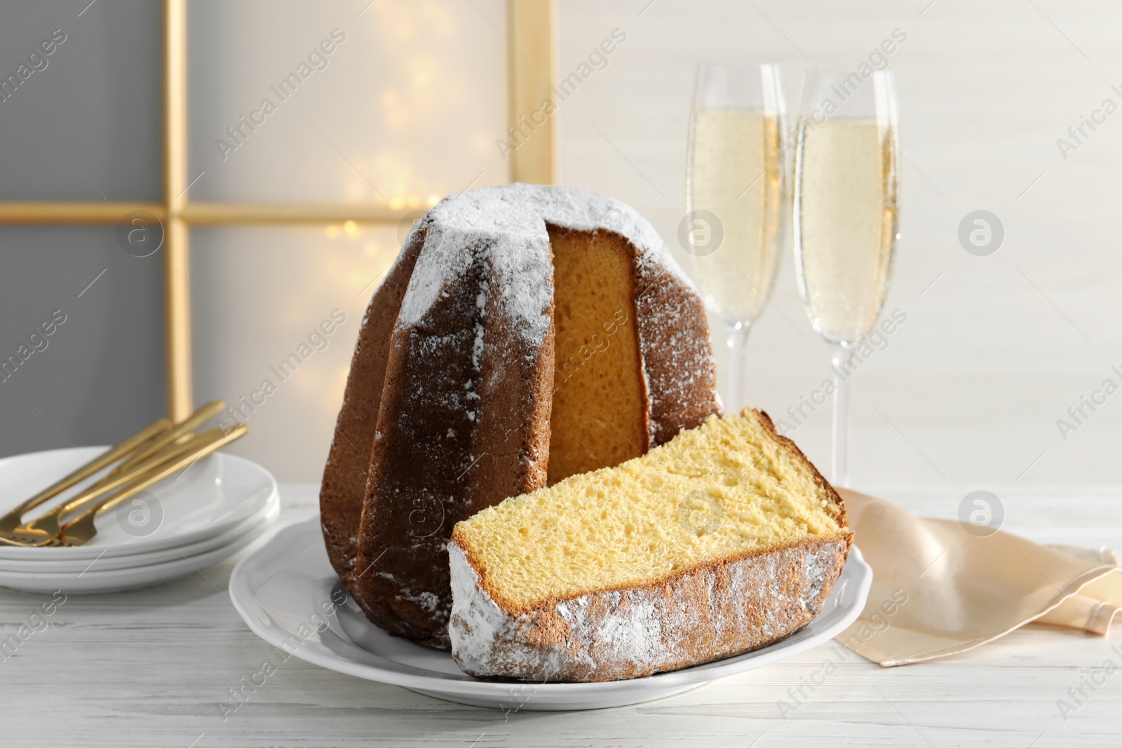 Photo of Delicious Pandoro cake decorated with powdered sugar and glasses of sparkling wine on white wooden table. Traditional Italian pastry