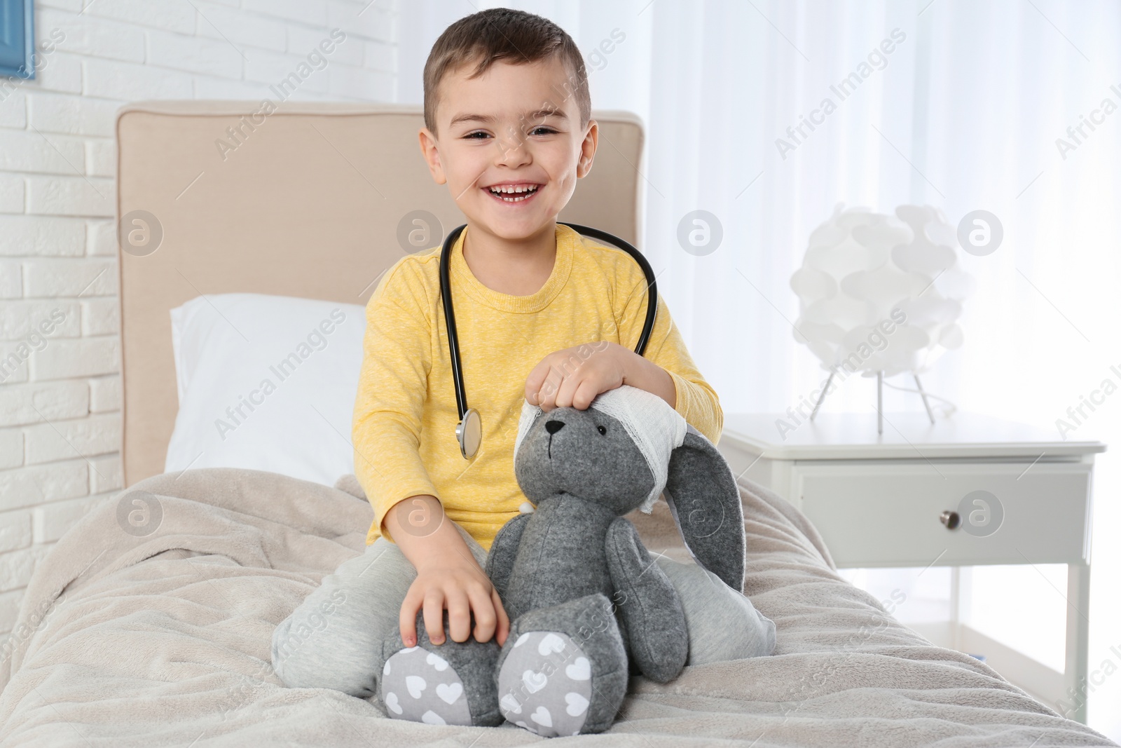 Photo of Cute child playing doctor with stuffed toy at hospital