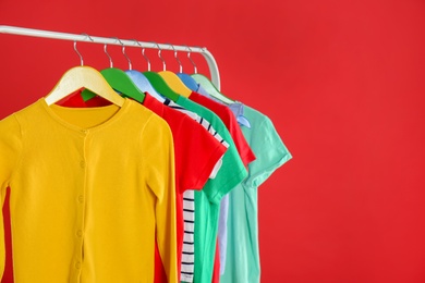Photo of Rack with stylish children clothes on red background. Space for text