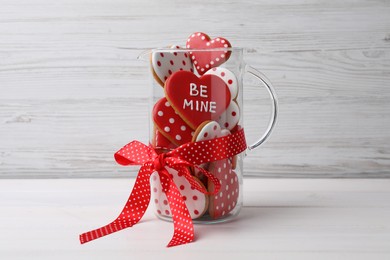 Photo of Delicious heart shaped cookies in glass jug with red bow on white wooden table
