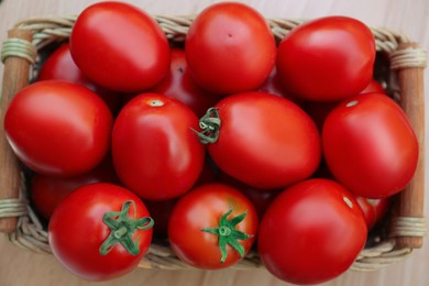 Photo of Wicker basket with fresh tomatoes on wooden table, top view