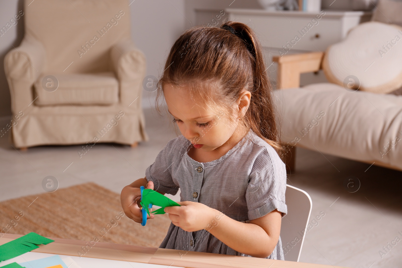 Photo of Little girl cutting color paper with scissors at table indoors