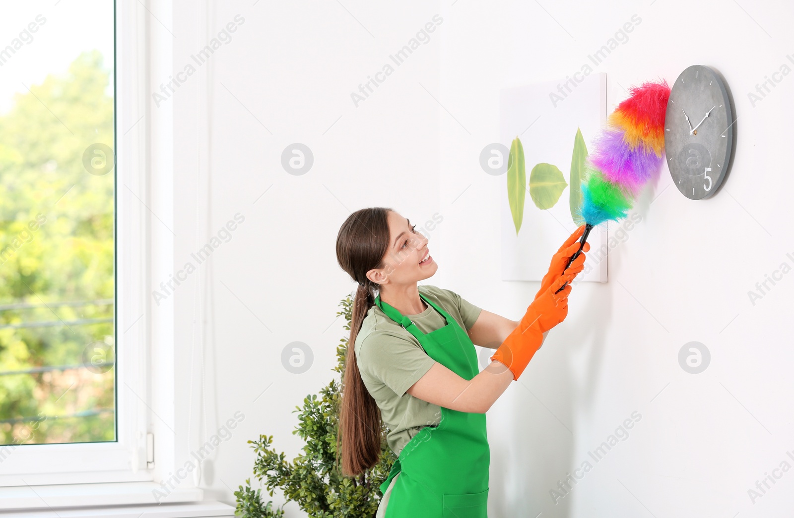 Photo of Young woman cleaning room with dusting brush indoors