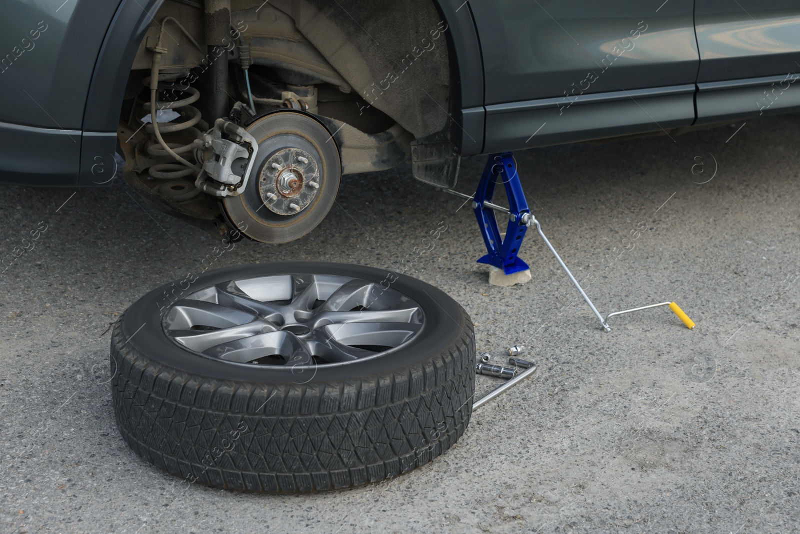 Photo of Car lifted by scissor jack and new wheel on asphalt outdoors. Tire puncture