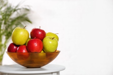 Photo of Bowl with different sweet apples on table indoors, space for text