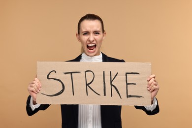 Photo of Screaming woman holding cardboard banner with word Strike on beige background