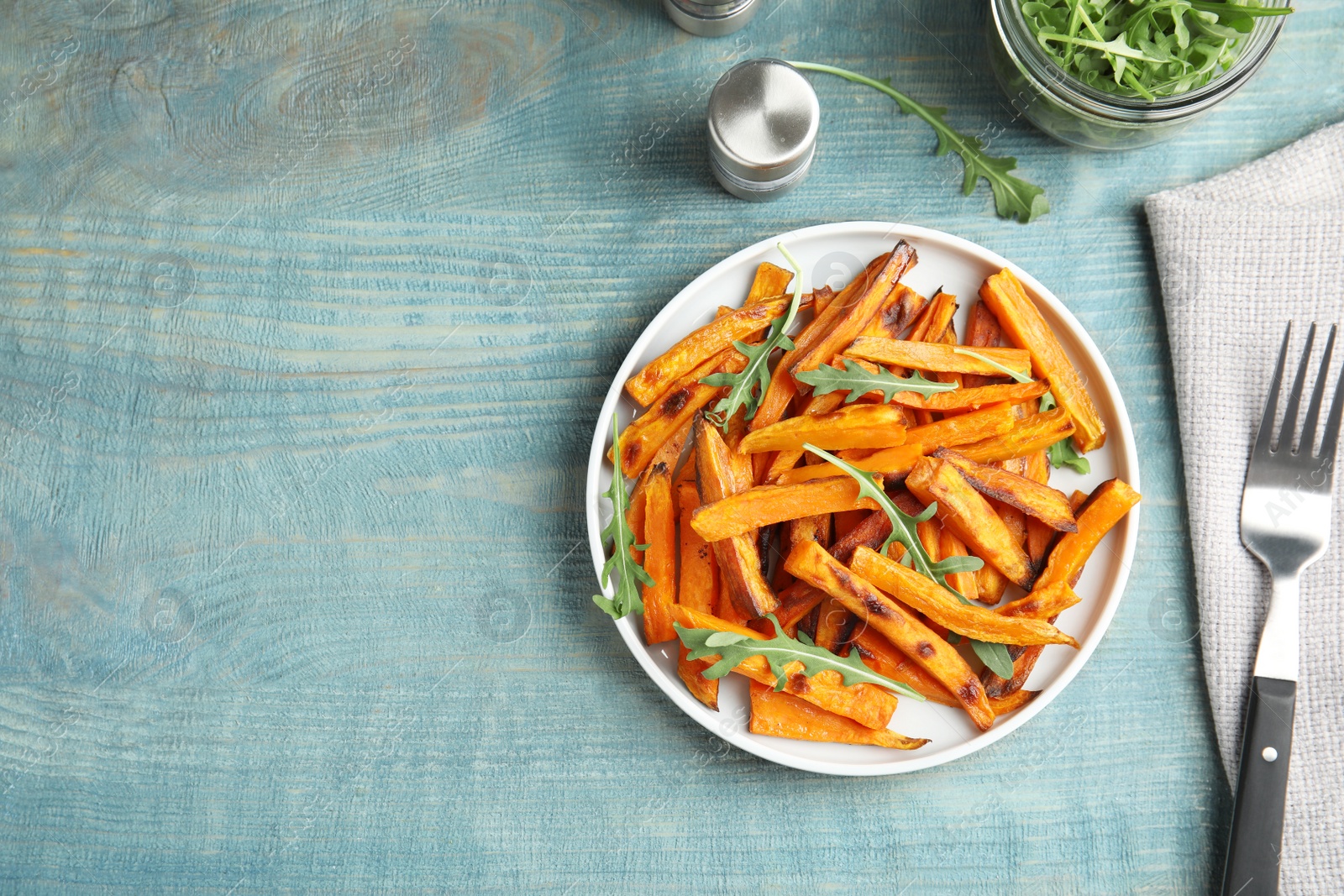 Photo of Plate with baked sweet potato slices and arugula served on wooden table, top view. Space for text