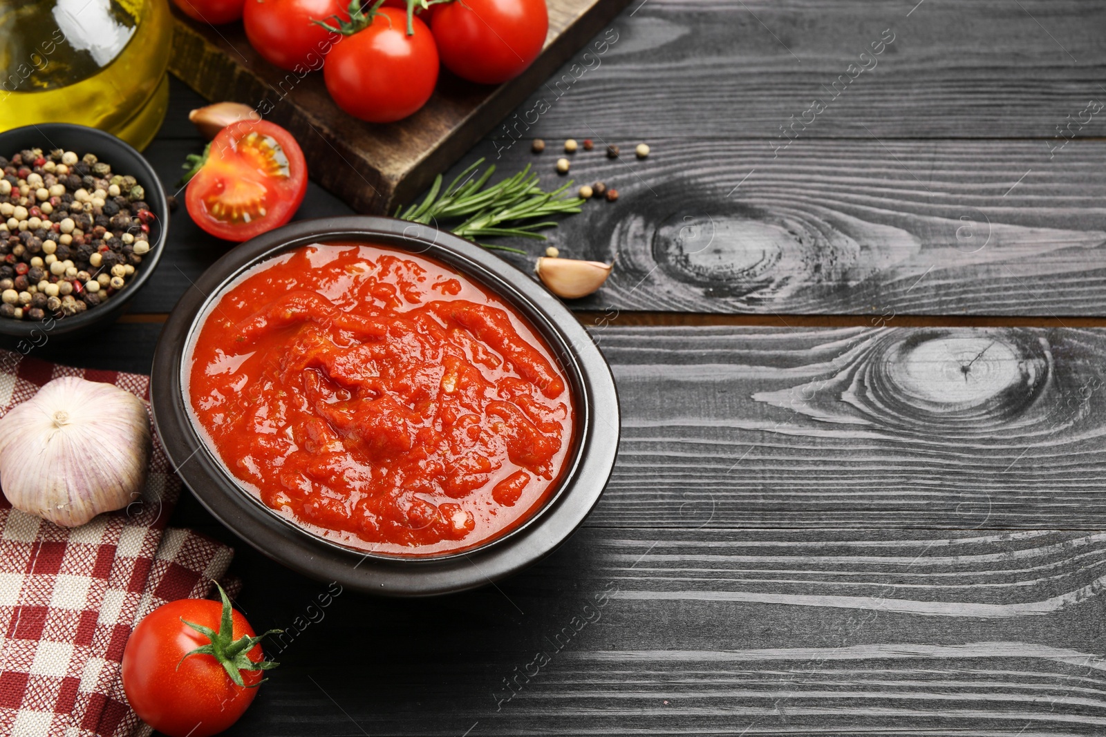 Photo of Homemade tomato sauce in bowl and fresh ingredients on black wooden table, space for text