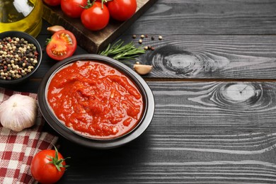 Homemade tomato sauce in bowl and fresh ingredients on black wooden table, space for text