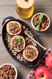 Photo of Tasty baked apples with nuts, honey and mint in baking dish on wooden table, flat lay