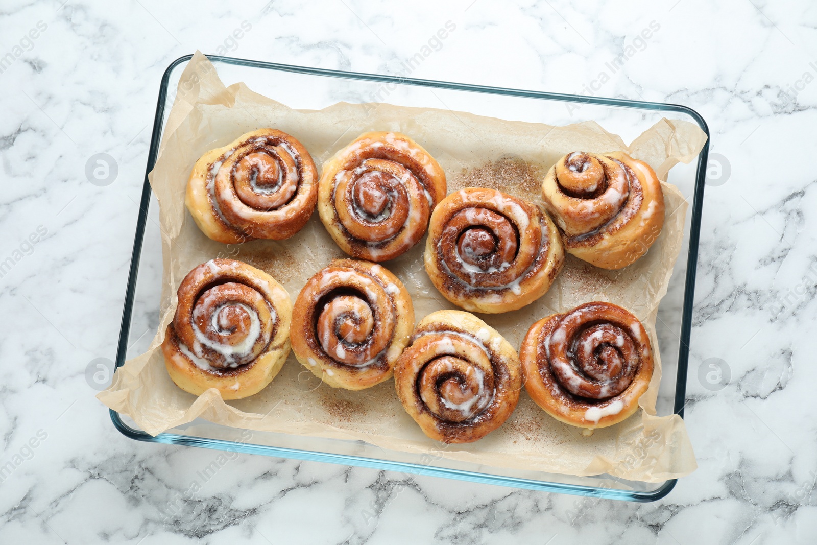 Photo of Baking dish with tasty cinnamon rolls on white marble table, top view