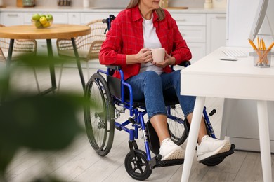 Photo of Woman in wheelchair with cup of drink using computer at home, closeup