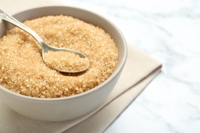 Photo of Brown sugar in bowl and spoon on white marble table, closeup. Space for text