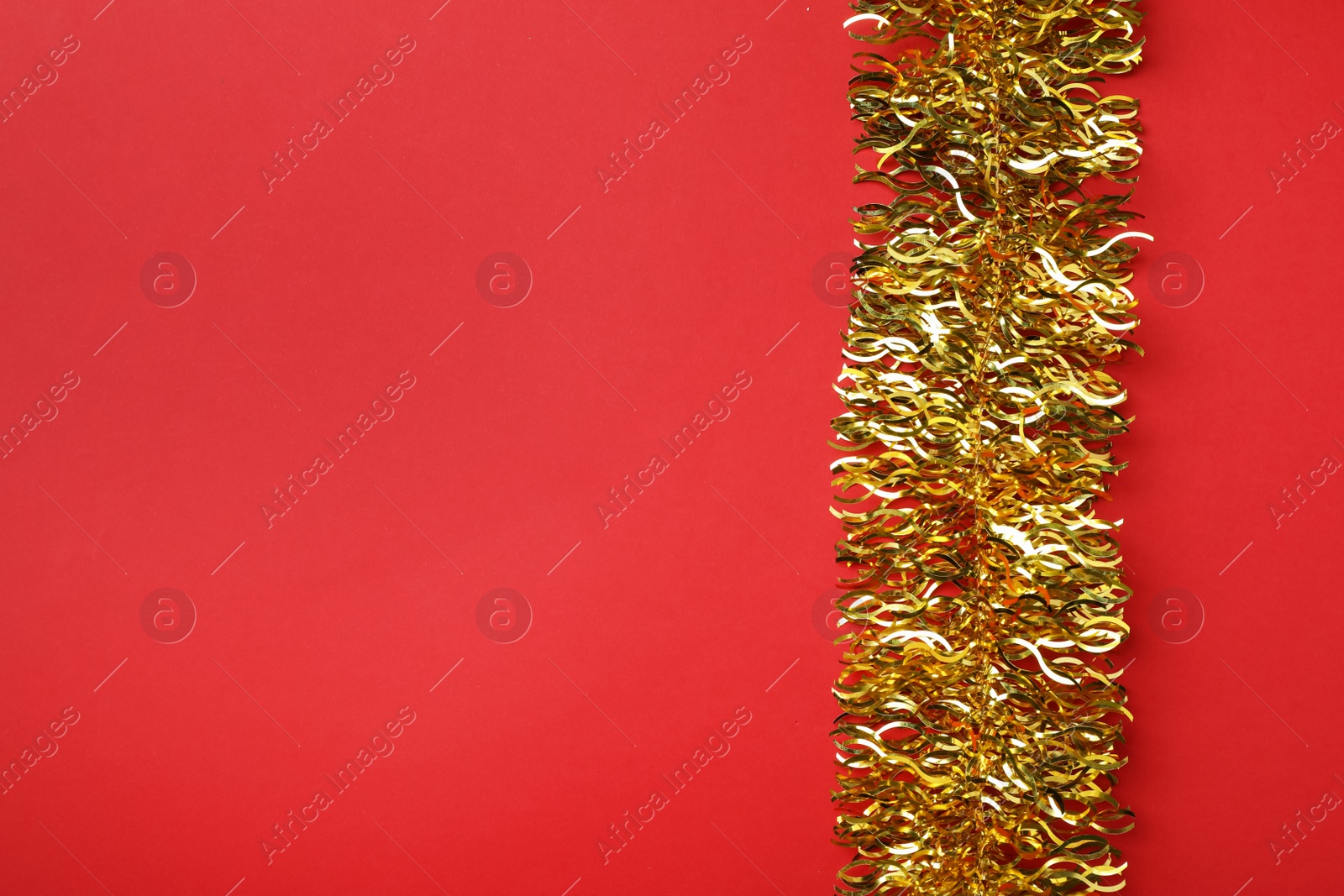 Photo of Golden tinsel on red background, top view. Space for text