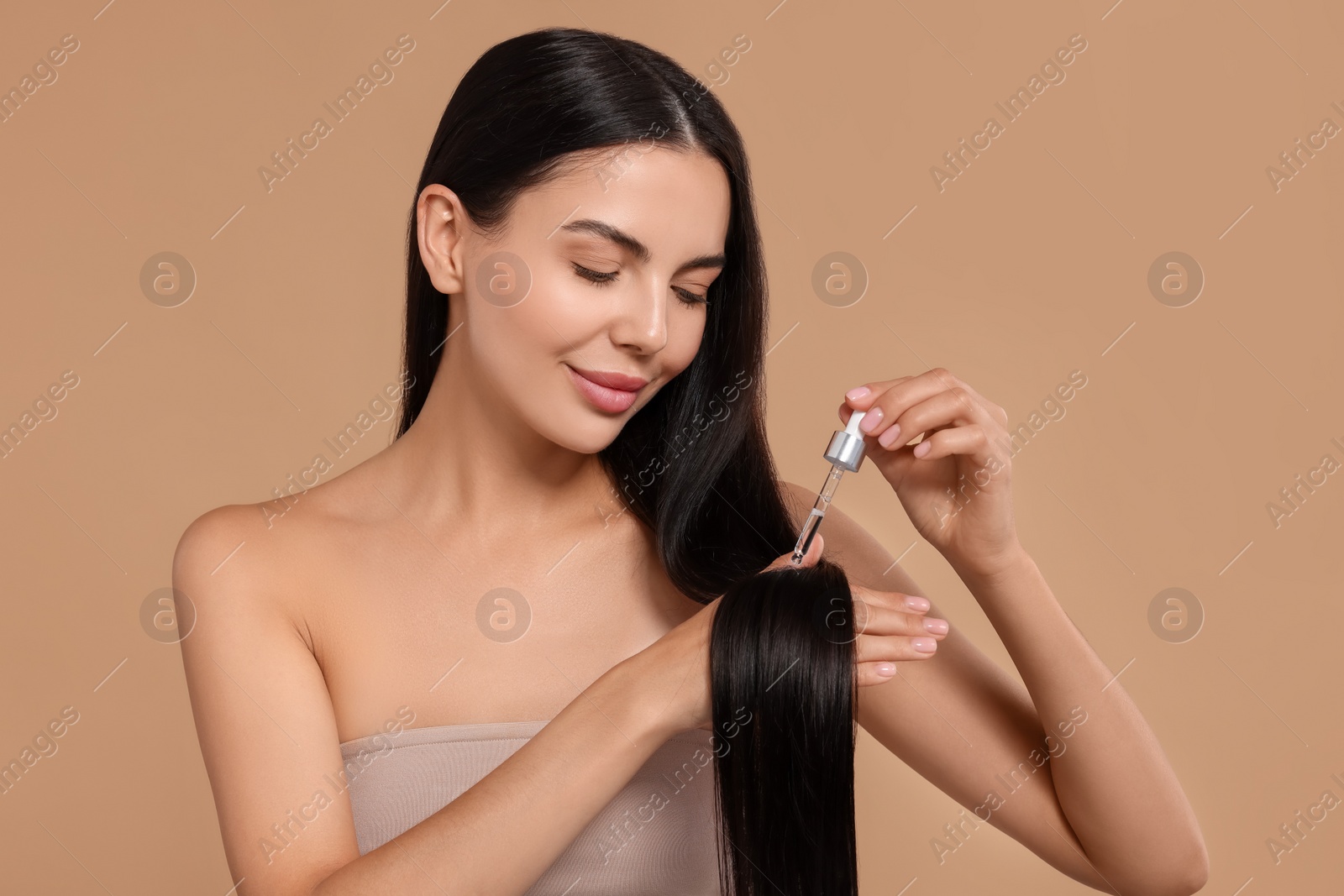 Photo of Beautiful woman applying hair serum on beige background. Cosmetic product