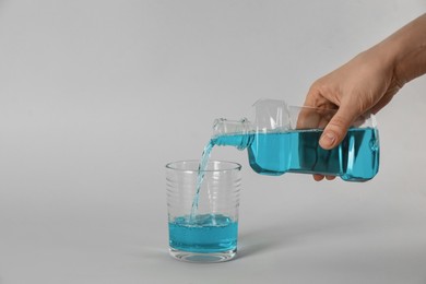 Photo of Woman pouring mouthwash into glass on light grey background, closeup