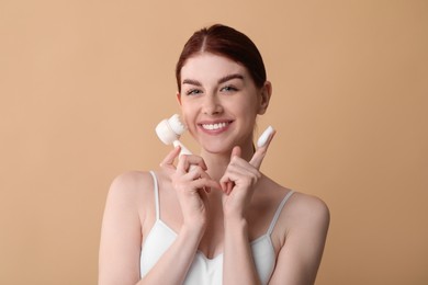 Photo of Washing face. Young woman with brush and cleansing foam on beige background