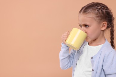Photo of Cute girl drinking beverage from yellow ceramic mug on beige background, space for text
