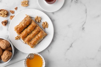 Eastern sweets. Pieces of tasty baklava, walnuts and tea on white marble table, flat lay. Space for text