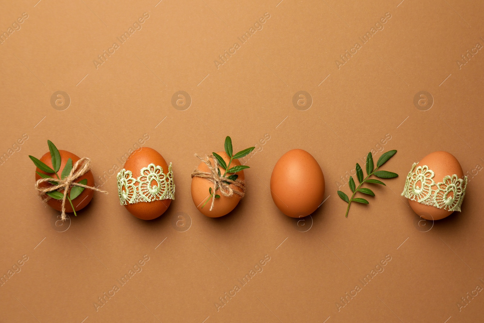 Photo of Festively decorated chicken eggs on brown background, flat lay. Happy Easter