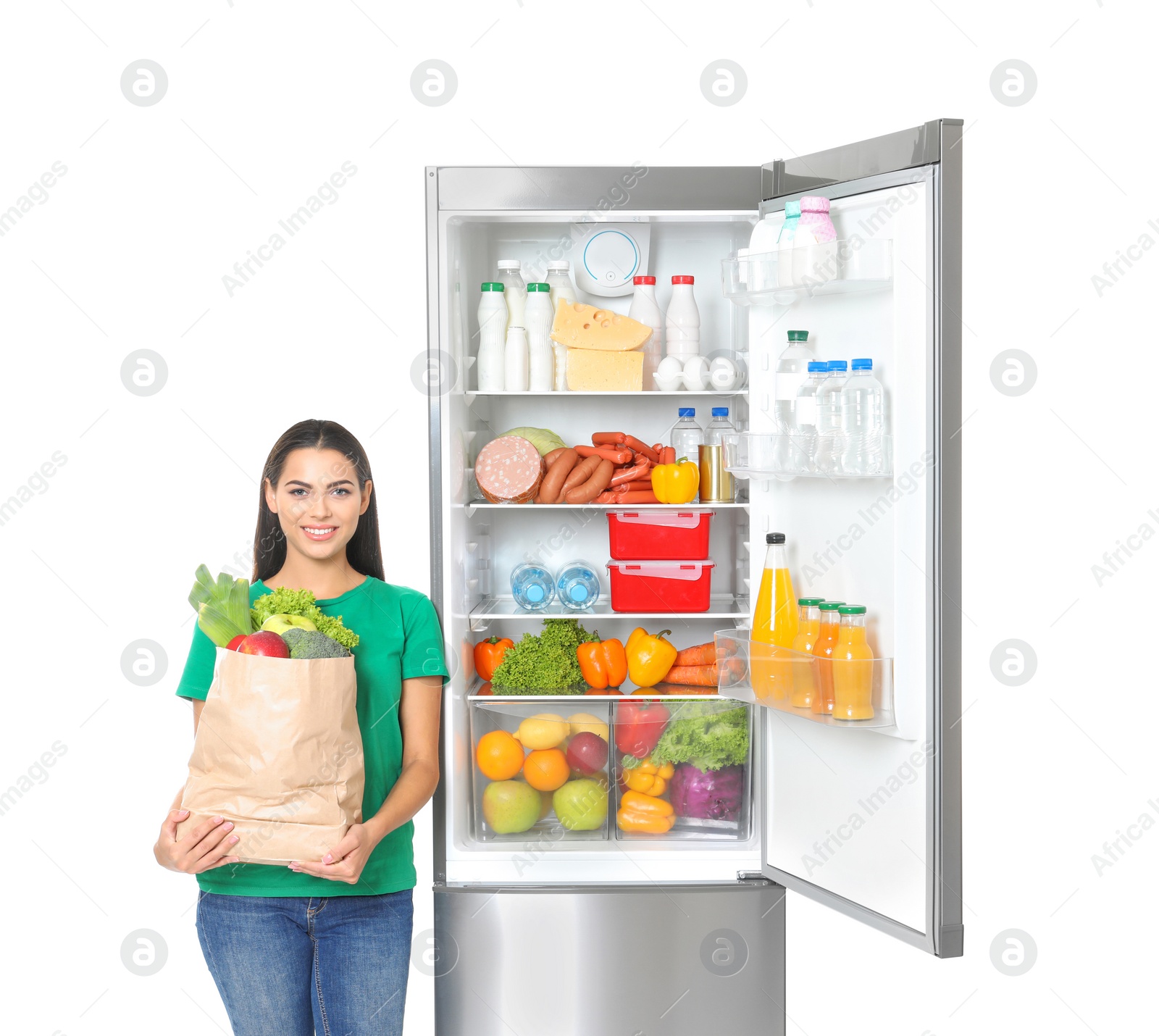 Photo of Young woman with bag of groceries near open refrigerator on white background