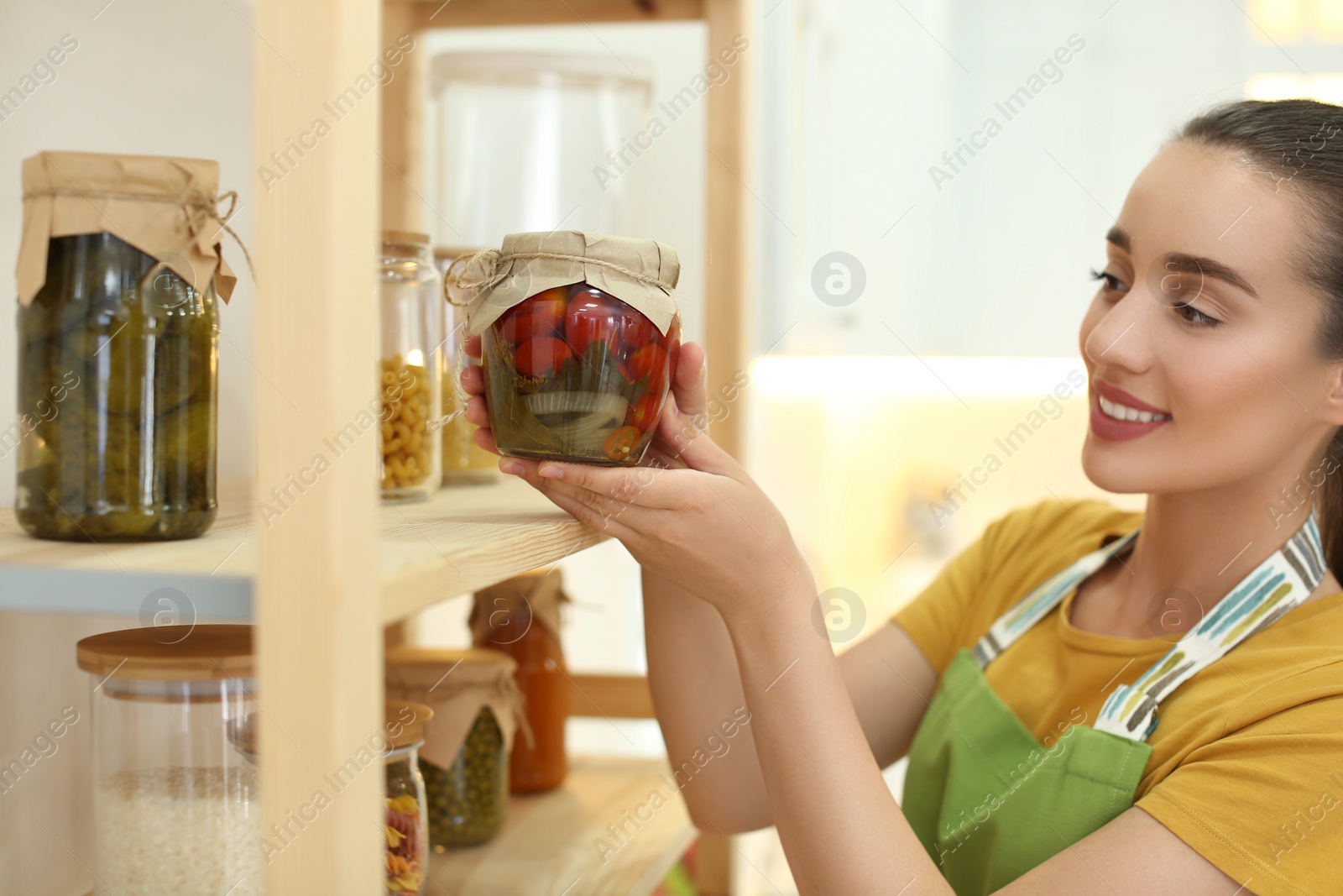 Photo of Woman putting jar of pickled vegetables on shelf indoors