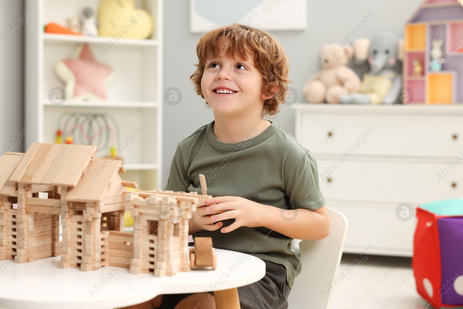 Photo of Little boy playing with wooden entry gate at white table in room. Child's toy