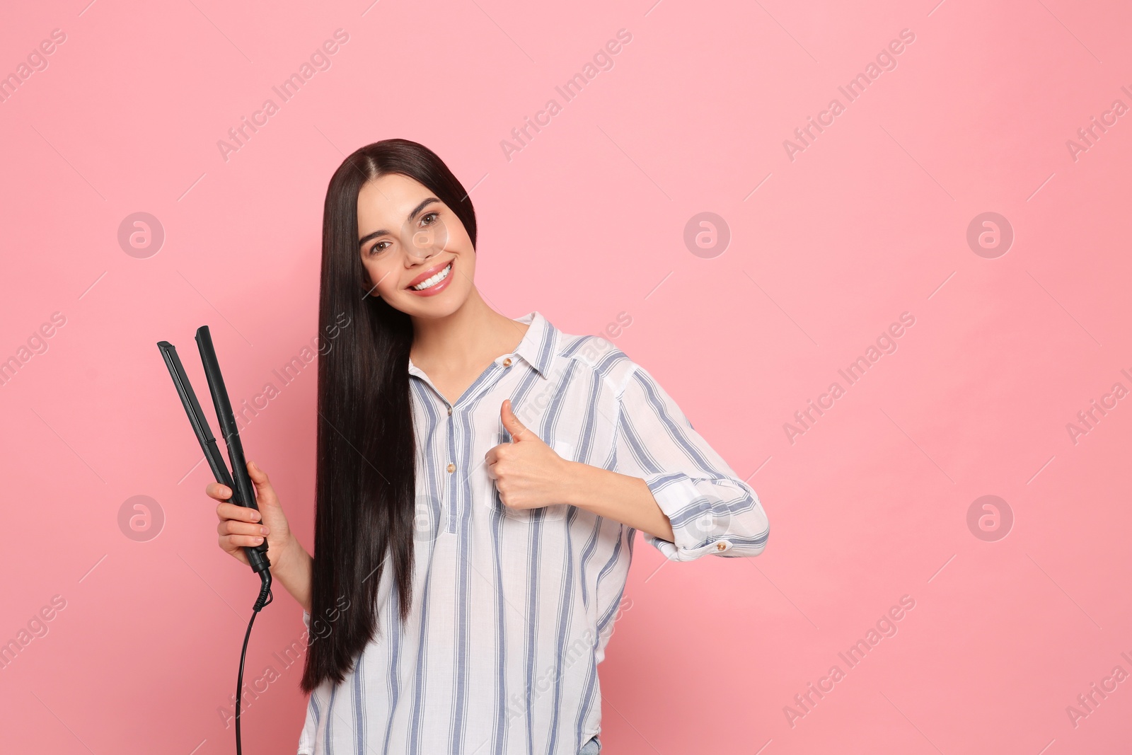 Photo of Beautiful happy woman with hair iron showing thumbs up on pink background. Space for text