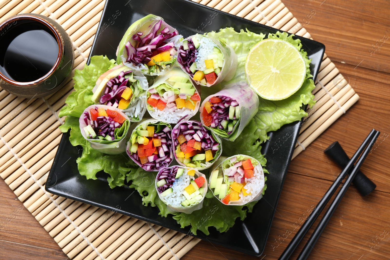 Photo of Delicious spring rolls, soy sauce and chopsticks on wooden table, top view