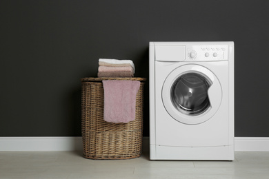 Photo of Modern washing machine and laundry basket near black wall