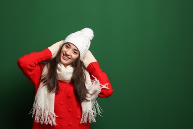 Young woman wearing warm clothes on color background, space for text. Winter season