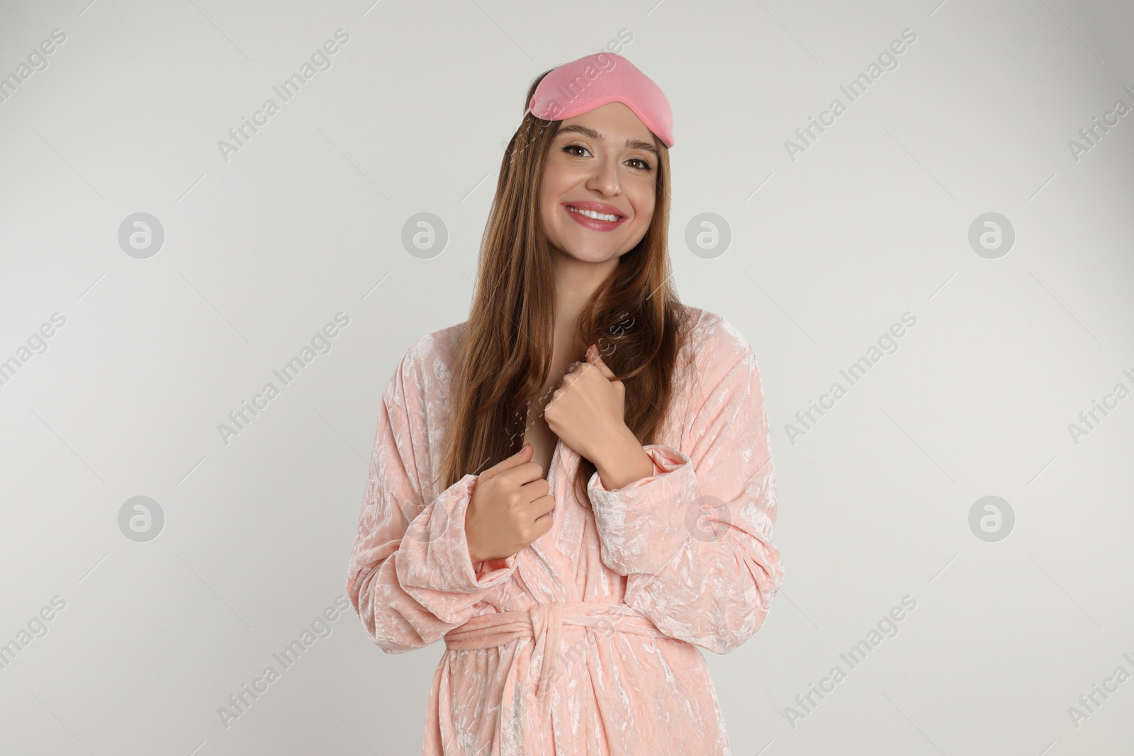Photo of Beautiful young woman in bathrobe and eye sleeping mask on light background