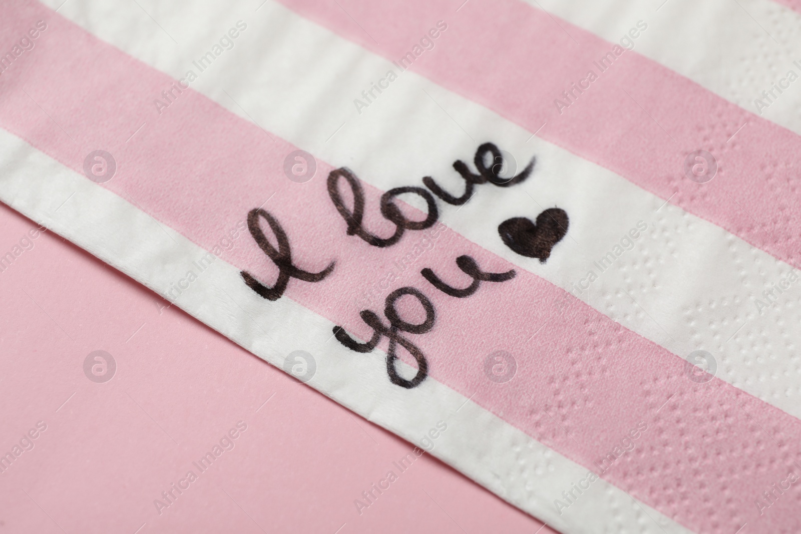Photo of Napkin with handwritten message I Love You on pink table