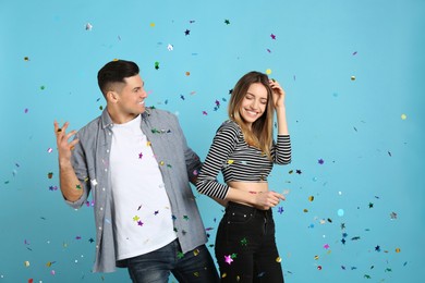 Photo of Happy couple and falling confetti on light blue background