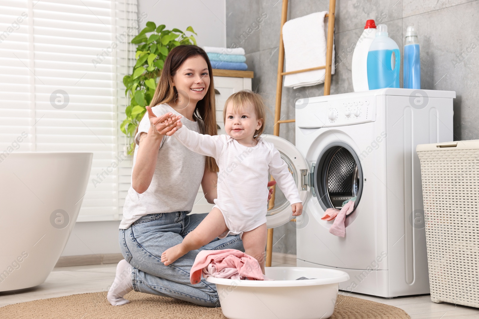 Photo of Happy mother with her daughter having fun while washing baby clothes in bathroom