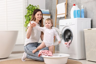 Happy mother with her daughter having fun while washing baby clothes in bathroom