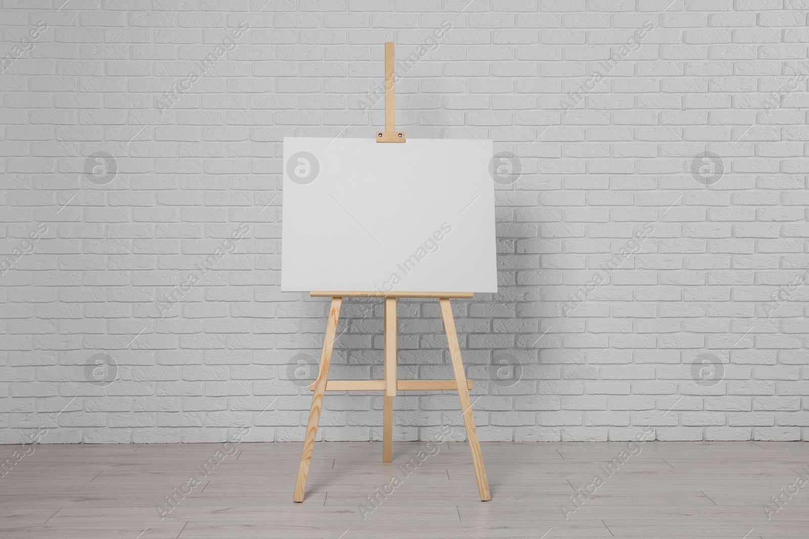 Photo of Wooden easel with blank canvas near white brick wall indoors