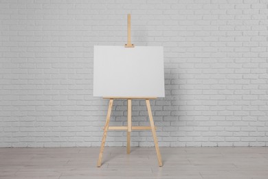 Wooden easel with blank canvas near white brick wall indoors