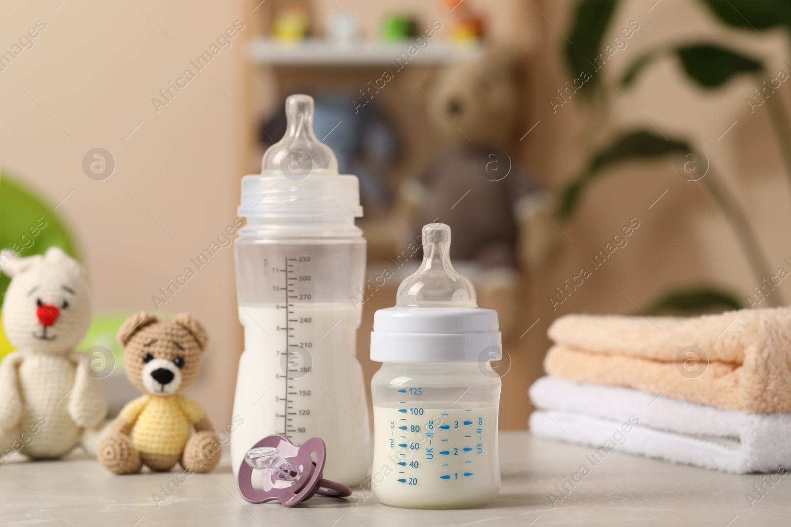 Photo of Feeding bottles with baby formula, pacifier, toys and towels on light grey table indoors